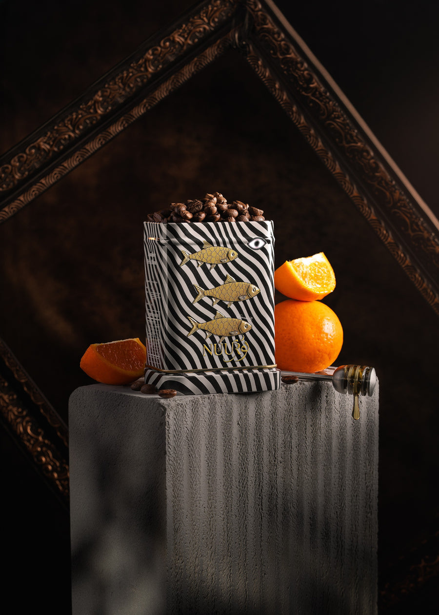 Manaima artwork tin filled with coffee beans beside oranges