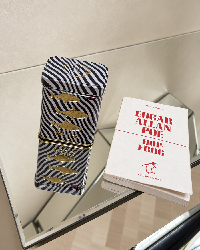 NUUR fish art tin beside a book on a mirrored table